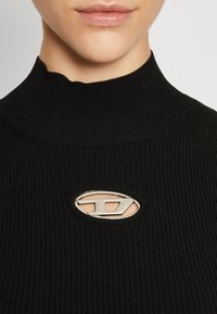 Schwarzer gerippter Rollkragenpullover mit einem Ausschnitt und silbernem Metallic-Akzent. Der Stoff ist strukturiert und eng anliegend mit einem hohen Kragen.