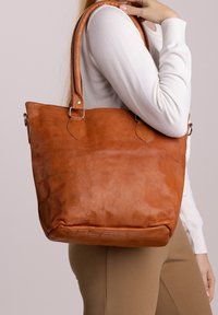 Borsa a spalla in pelle marrone con una forma strutturata, manici corti e accessori in metallo. Mostra una texture naturale e una finitura morbida.