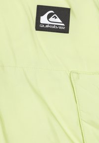 Lys grønn Quiksilver vindjakke laget av glatt nylon. Har et svart logomerke og stiftede sømdetaljer. Minimalistisk design.