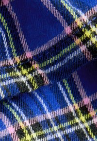 Tessuto a quadri blu e nero con accenti rosa e verdi, superficie morbida e testurizzata con un motivo intrecciato di larghezze variabili.