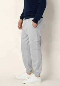 Grå sweatpants i mjukt tyg med sidofickor och elastiska muddar, kombinerat med vita sneakers och en marinblå sweatshirt.