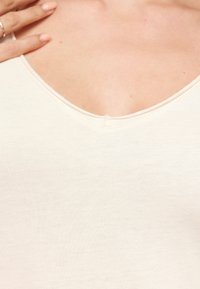 Beige, přiléhavý top s výstřihem do V, vyrobený z hladkého, lehkého materiálu, s jemnou strukturou a minimálními švy v oblasti výstřihu.