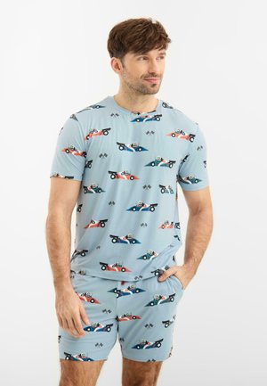 Mand iført lyseblå matchende skjorte og shorts med mønstre af racerbiler i rød, blå og grøn samt ikoner af ternede flag.