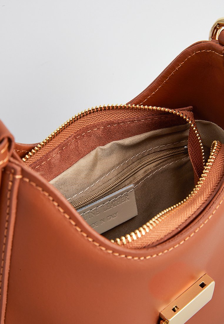 Intérieur d'un sac à main en cuir tan avec une fermeture éclair dorée, doté d'une doublure en tissu et d'une petite poche zippée pour l'organisation. Accent matériel visible.
