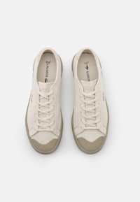 Baskets en toile beige avec une semelle en caoutchouc, un bout rond et un laçage à l'avant ; présentent un embout texturé beige et un petit logo sur le côté.