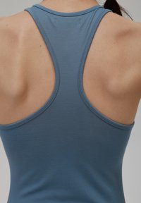 Niebieski sportowy top bez rękawów z wycięciem na plecach. Wykonany z gładkiego, elastycznego materiału, z delikatnymi szwami i dopasowanym krojem.