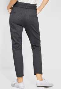 Šedé slim-fit kalhoty vyrobené z texturované tkaniny, s plochým pasem, zadními kapsami a zkrácenou délkou, spojené s bílými teniskami.