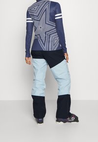 Marinblå långärmad topp med stjärnmönster och vita ränder, kombinerad med ljusblå och marinblå skidbyxor. Slät textur, funktionell design.