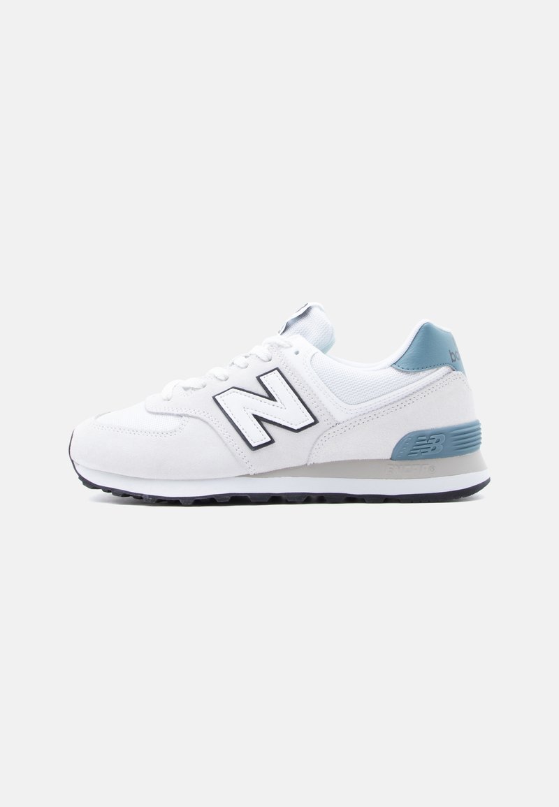 Λευκό και ανοιχτό μπλε αθλητικό παπούτσι New Balance με μαύρο λογότυπο, κορδόνια και υφή μαύρης σόλας, εμφανιζόμενο από το πλάι σε λευκό φόντο.