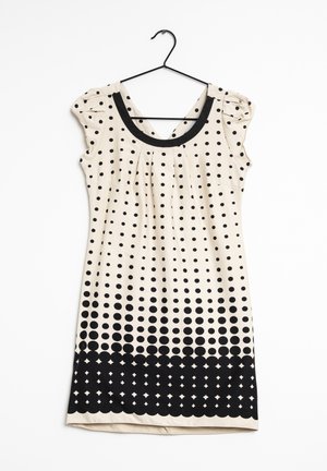 Abito smanicato color crema con pois neri che sfumano in un motivo a punti densi vicino all'orlo, appeso a una gruccia nera.