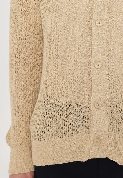 Beige strikket cardigan med lett, teksturert stoff, lange ermer og seks runde knapper foran.