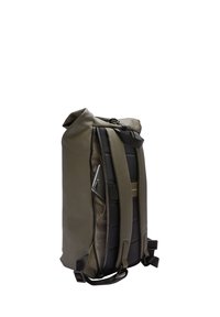 Sac à dos en nylon vert olive avec un système de fermeture enroulable, un dos rembourré, des bretelles ajustables et une poche latérale contenant un smartphone.