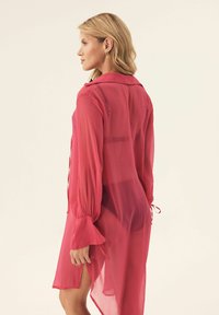 Przezroczysta, różowa długa sukienka z kołnierzykiem, długimi rękawami i wiązaniami w talii, o prostym kroju i bocznych rozcięciach.