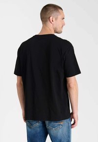 Camiseta de algodón negra con un corte relajado y cuello redondo, con mangas cortas y una textura suave, combinada con jeans de mezclilla azules.