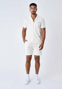 Camicetta bianca a maniche corte e pantaloni corti abbinati con texture a righe verticali. Presenta un colletto e chiusure con bottoni. Abbinata a sneakers bianche.