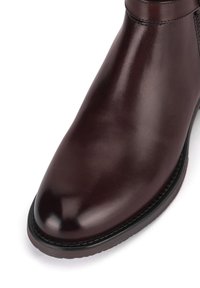 Burgundowe skórzane botki za kostkę o gładkiej, wysokopołyskowej powierzchni, zaokrąglonym nosku oraz subtelnym przeszyciu przy kołnierzu i podeszwie.