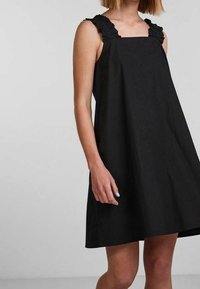 Svart ärmlös klänning med volangiga axelband, lös A-linjeformad siluett och slät tygtextur. Enkel och stilren design.