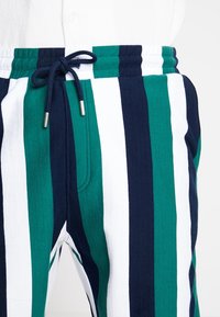 Pantalon rayé aux couleurs bleu marine, vert et blanc. Confectionné dans un tissu doux avec une taille élastique et un cordon de serrage pour un ajustement optimal.