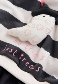 Tessuto a righe grigio e bianco con un fantasmino morbido decorato da motivi floreali rosa e un cappello nero, accompagnato dal testo "niente scherzi, solo avventure."