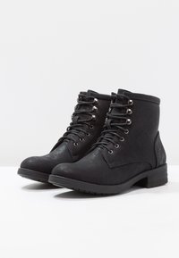 Botas de tobillo negras con cordones, hechas de cuero sintético texturizado, con herrajes plateados, un tacón bajo apilado y un diseño de punta redondeada.