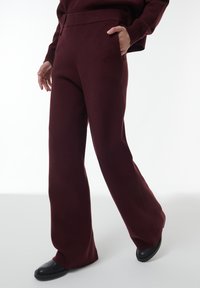 Bordeaux wijdpijpenbroek van zacht materiaal, met een hoge tailleband en zijzakken, gecombineerd met zwarte platte schoenen.