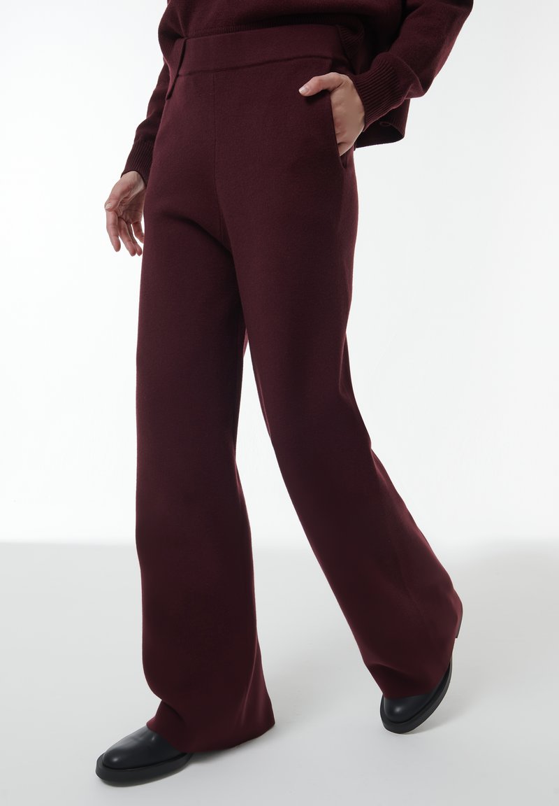 Bordeaux wijdpijpenbroek van zacht materiaal, met een hoge tailleband en zijzakken, gecombineerd met zwarte platte schoenen.