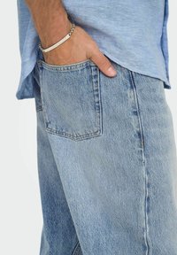 Ljusblå denimjeans med rak passform, med en sidoficka och minimal synlig sömnad. Bärs med en ljusblå skjorta.