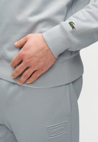 Γκρι φούτερ με ριμπ τελειώματα, διακοσμημένο με κεντητό πράσινο λογότυπο κροκοδείλου στο μανίκι και υφασμάτινο λογότυπο με υφή στη μέση.