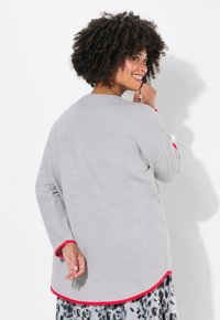 Maglione grigio a maniche lunghe con rifiniture rosse, vestibilità rilassata e orlo arrotondato. Abbinato a una gonna a fantasia, visto da dietro.