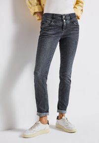 Mörk denimjeans med smal passform, som har två framfickor, två bakfickor och uppvikta muddar. Matchas med vita sneakers.