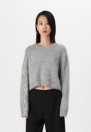 Cropped sweater in silver, textured with fuzzy fibers. Features a round neckline and long sleeves, paired with black trousers.