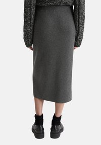 Jupe midi en laine grise avec une taille ajustée, texture lisse et coupe droite, associée à des chaussures à semelle épaisse noires et des chaussettes côtelées.