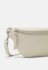 Borsa a tracolla in pelle crema con forma arrotondata, zip in argento e tracolla regolabile. Presenta un branding sottile impresso sul lato.
