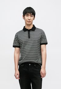 Polo cinzenta com padrão, gola e mangas pretas, com botões frontais. Usada com jeans escuros. Textura suave, design moderno.