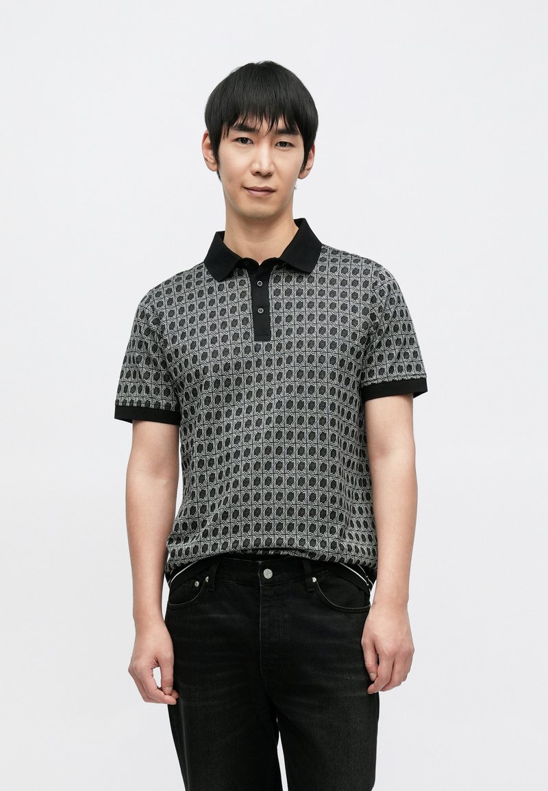 Polo cinzenta com padrão, gola e mangas pretas, com botões frontais. Usada com jeans escuros. Textura suave, design moderno.