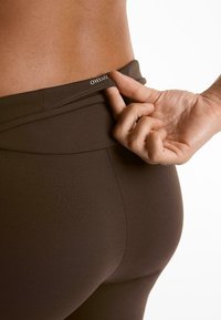 Brown high-waisted leggings made from stretch fabric. Tag visible at the waistband with brand name. Smooth texture and fitted design.