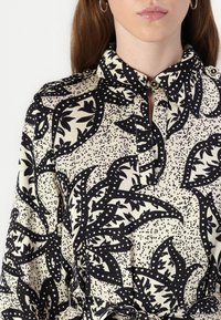 Camicia a fantasia nera e crema con colletto, dettagli con bottoni e un design floreale con dettagli a pois su un tessuto morbido.