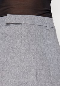 Pantalon gris en tissu texturé. Il présente une ceinture plate avec une seule passants de ceinture et des plis marqués à l'avant.