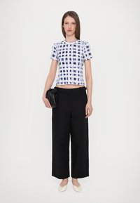 White and blue tie-dye cropped top, black wide-leg trousers, and white pointed flats, paired with a black handbag. Smooth fabrics and structured design.