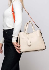 Borsa a tracolla beige con texture, dotata di due manici superiori e di una tracolla arancione staccabile. Presenta una tasca frontale e dettagli in metallo argentato.