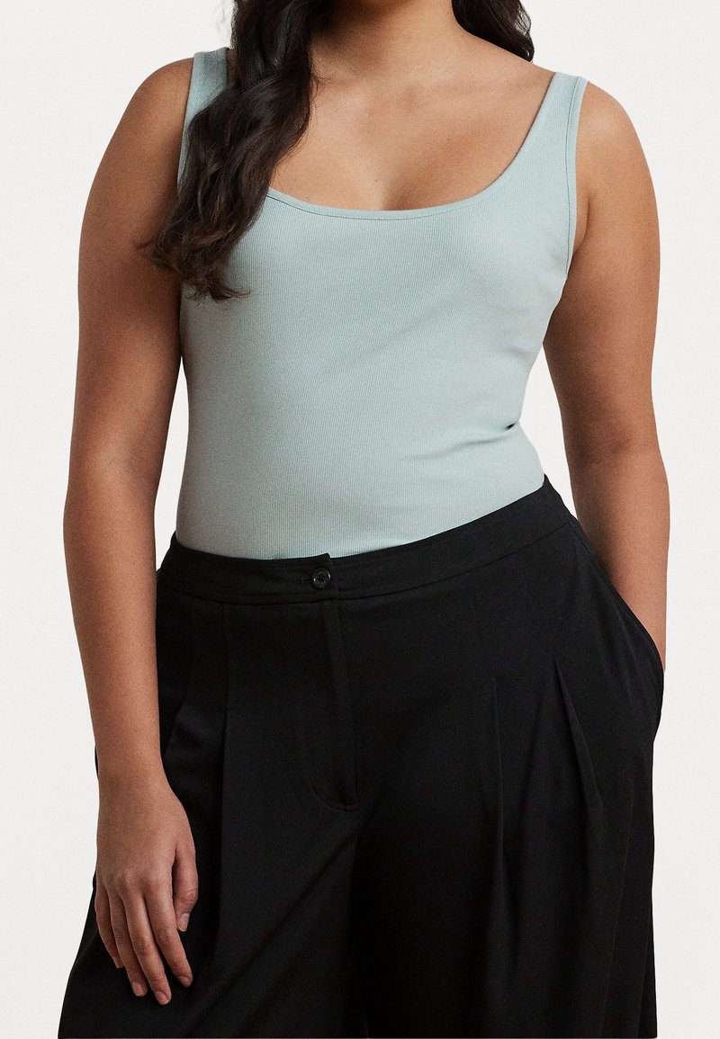 Top de tirantes ancho azul claro con textura acanalada, combinado con pantalones negros plisados de tiro alto, con bolsillos laterales y cierre de botones.