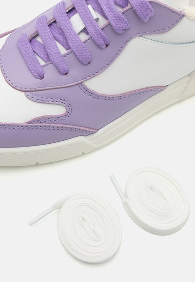 Lila och vit sneaker med överdel i texturerat läder, accentuerad sömnad och matchande lila snören. Två vita runda skosnören visas nedan.