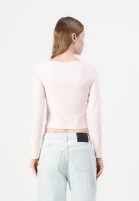 Langermet, tettsittende topp i lys rosa bomull, med firkantet utringning og cropped hem. Kombinert med lyseblå jeans med subtil tekstur.