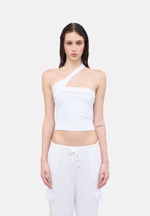 Crop top bianco a spalla singola con design aderente e texture liscia. Abbinato a pantaloni larghi in lino bianco con coulisse e tasche laterali.