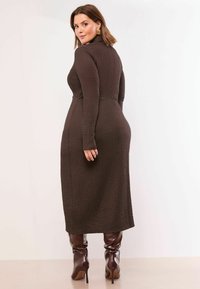 Brązowa sukienka midi z długim rękawem, o fakturowanym wzorze i dopasowanej talii, zestawiona z połyskującymi brązowymi kozakami za kolano z ostrymi noskami.
