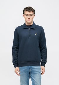 Tumesinine pehme kangast pullover, millel on pool-zäiega krae ja väike kuldne logo rinnal. Kergelt istuv lõige koos soonikkoes varrukaotstega.