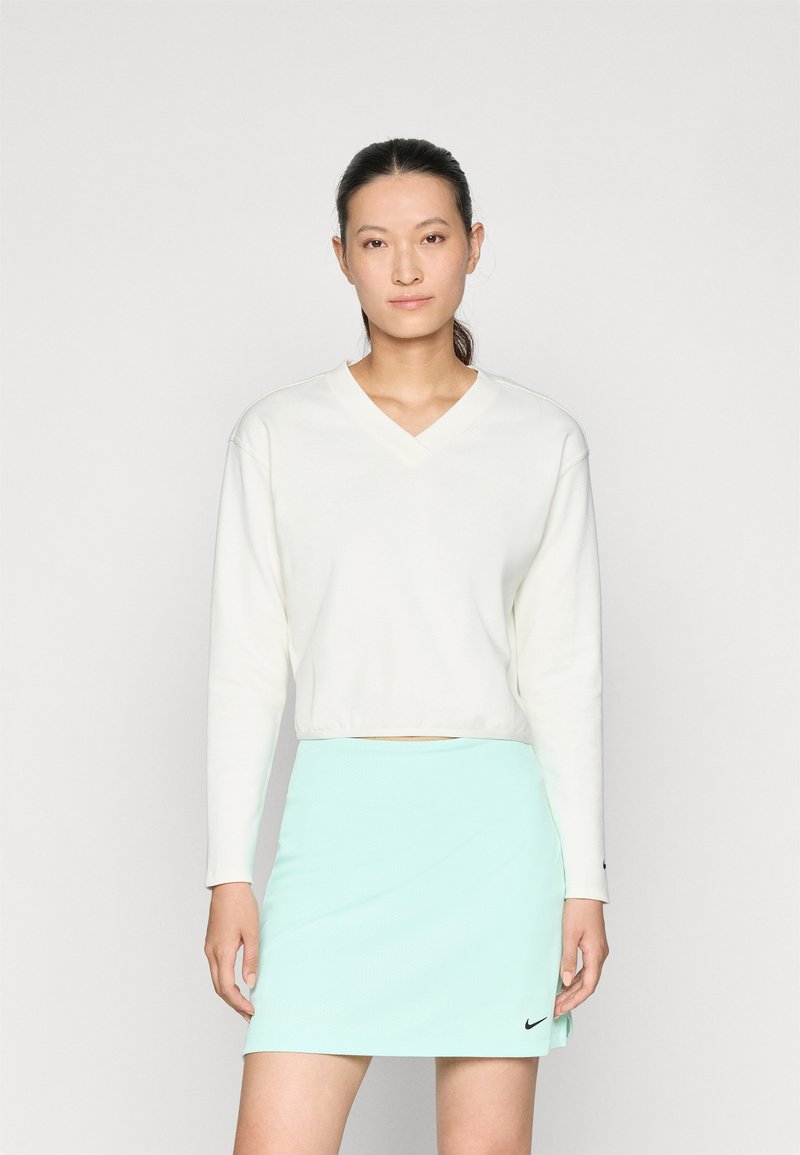 Λευκή κοντή μακρυμάνικη μπλούζα με V-λαιμόκοψη, συνδυασμένη με μια ανοιχτή μέντα πράσινη φούστα που διαθέτει το μαύρο λογότυπο της Nike στο στρίφωμα. Λαμπερή υφή, απλός σχεδιασμός.