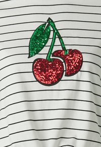 Camisa blanca con rayas negras que presenta un diseño de cerezas decorado con lentejuelas rojas y verdes. Las cerezas tienen hojas verdes y una textura brillante.