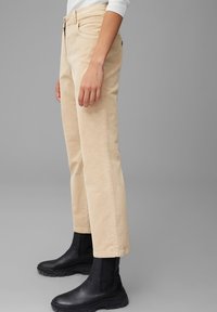 Beige corduroy broek met een rechte pijp, voorzien van achterzakken en een middelhoge taille, gecombineerd met zwarte elastische enkellaarzen.