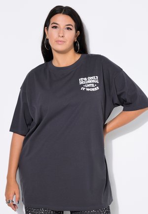 Übergrößes, dunkelgraues T-Shirt aus weichem Baumwollmaterial, mit weißem Text "Es ist nur illusorisch, bis es funktioniert" auf der linken Brust. Klassischer Rundhalsausschnitt.